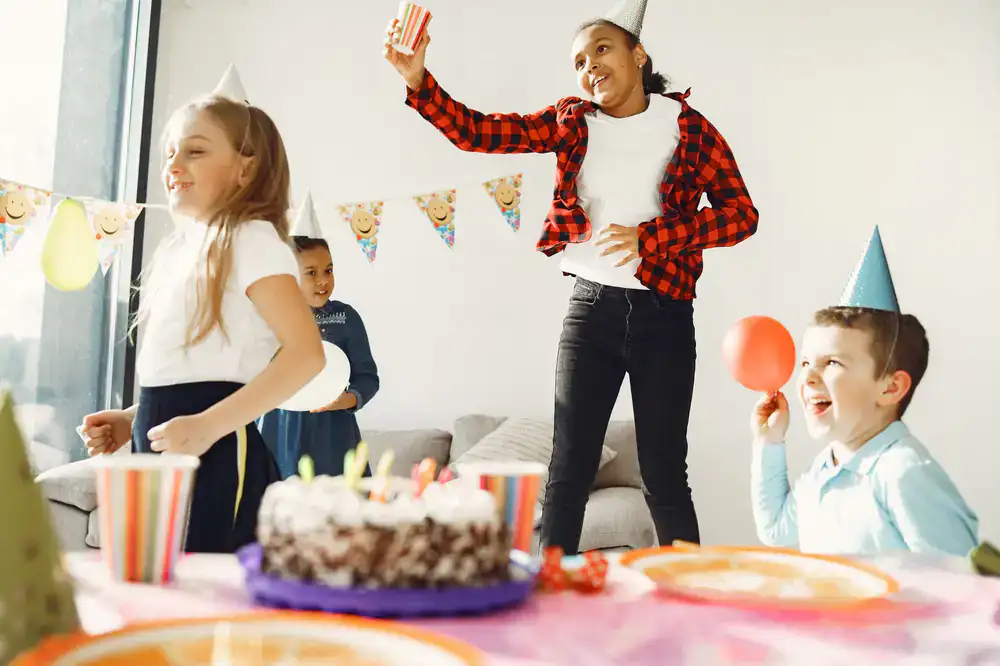 Group of smiling kids enjoying a birthday party with cake and balloons